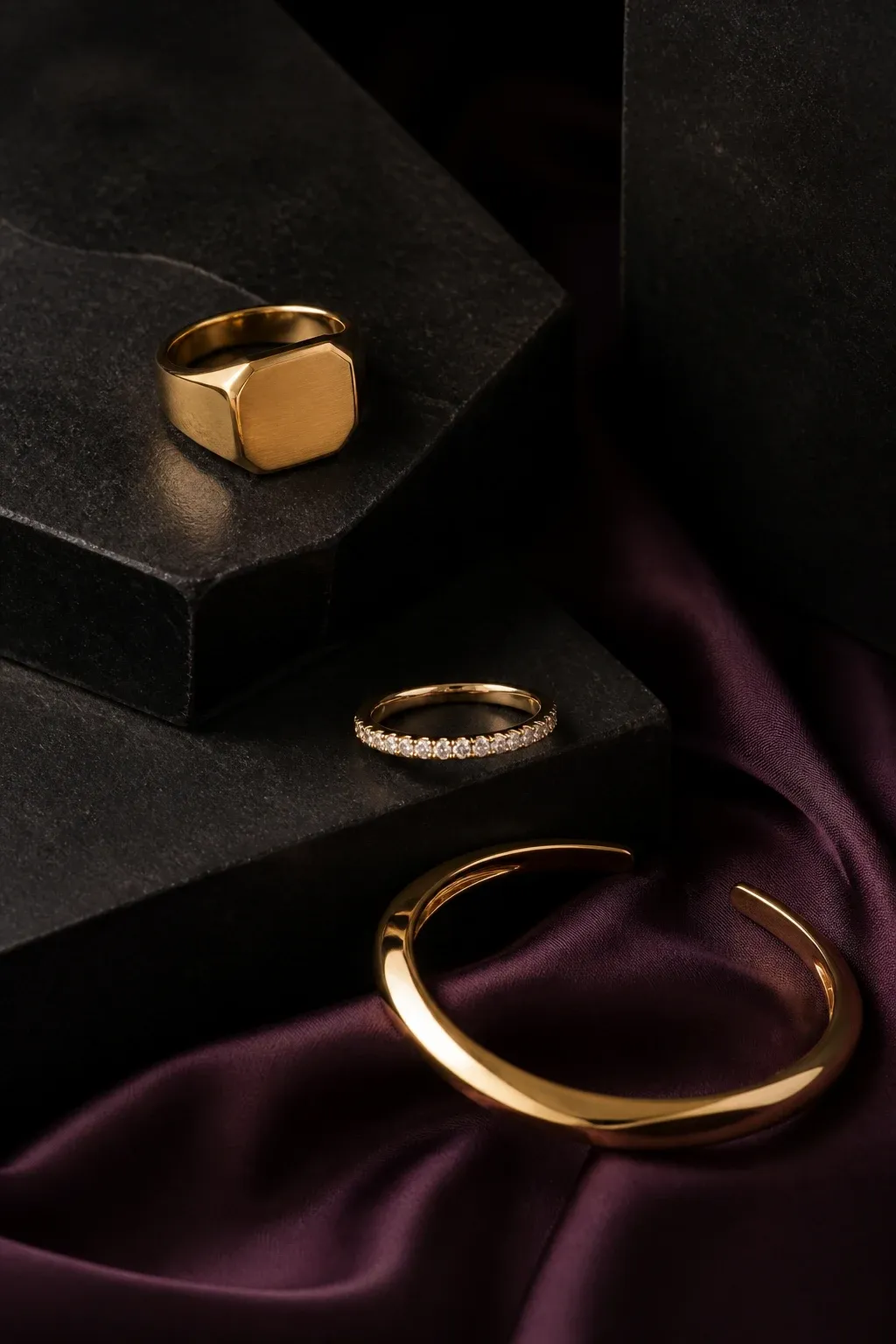 Sculptural gold jewelry arranged on black stone and aubergine silk